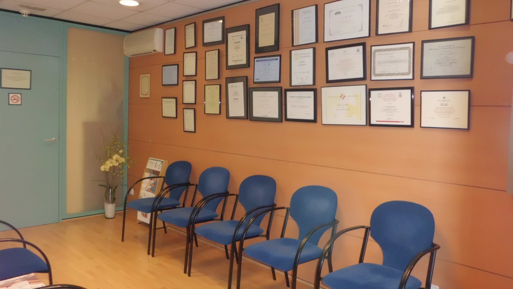 Sala de espera con pared en tono cálido y diplomas enmarcados